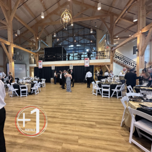 An indoor event space. It is decorated with many string lights, black curtains, and large white round tables with white linens for seating.