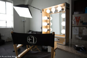 A photo of a room with a directors chair, a production light, and a hair and makeup mirror used for film productions set on a table.