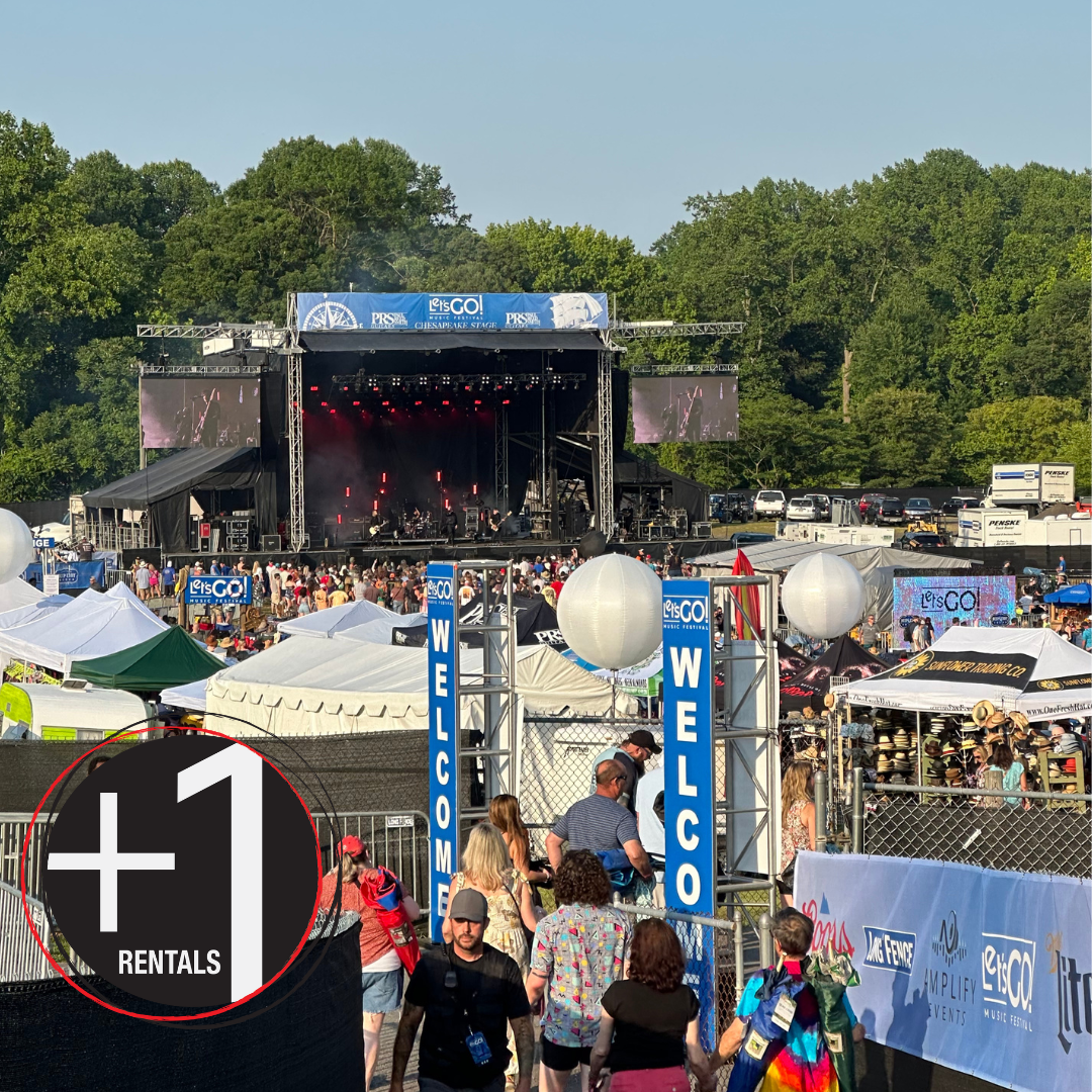 A photo of an outdoor festival space. There are people in line in the foreground, a large stage, trees, and vendors with their tents.